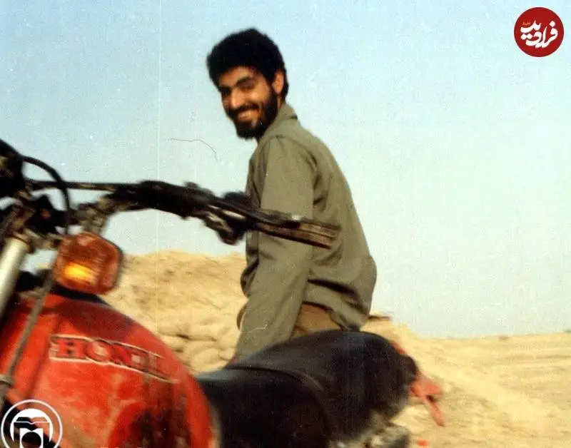 عکس؛ سفر به تاریخ؛ چهرۀ خندان «سردار سلیمانی» در کنار موتورسیکلتش در جبهه؛ دهۀ 60